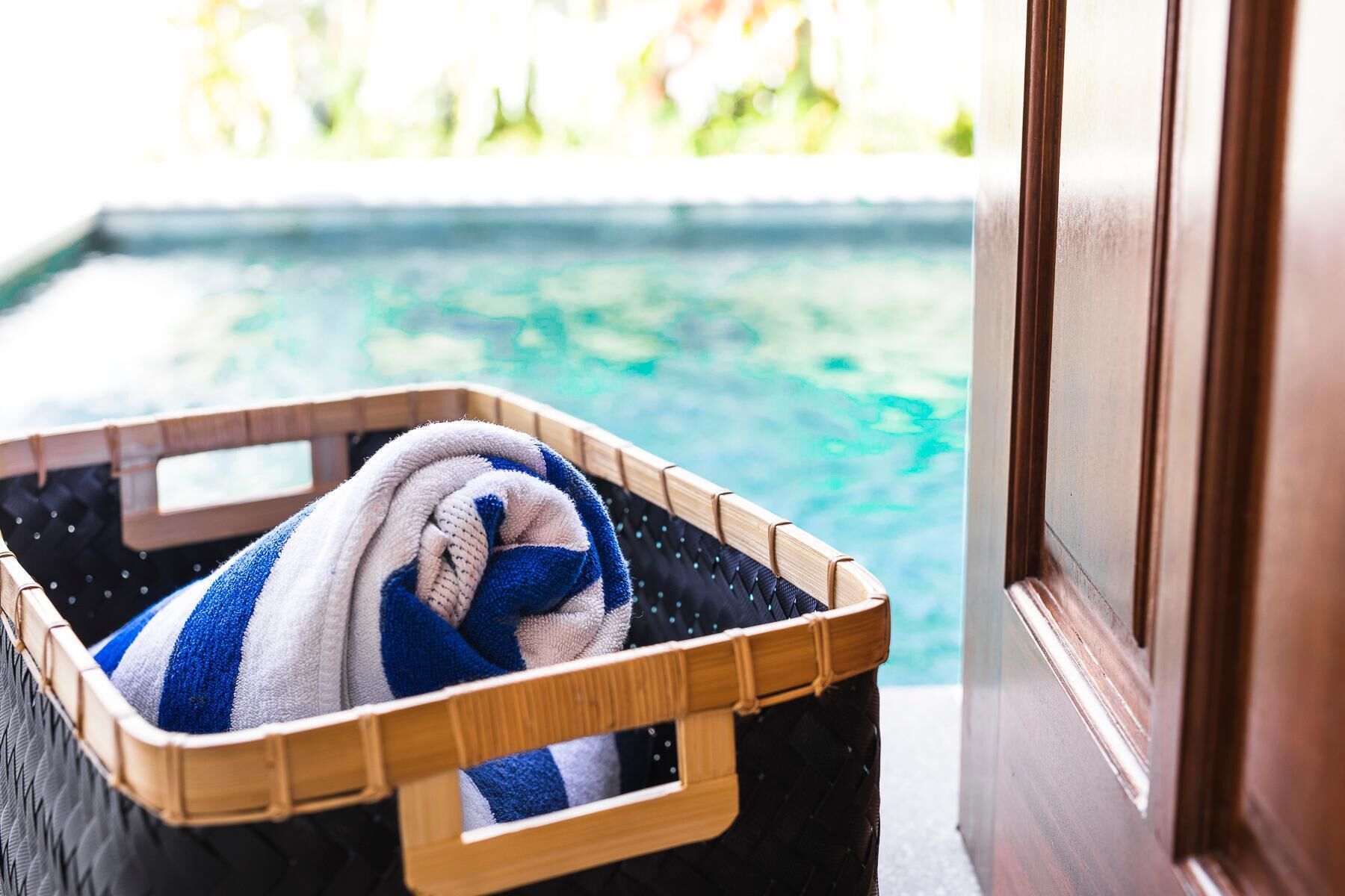 A wooden suitcase with a striped towel inside, placed near a poolside door.