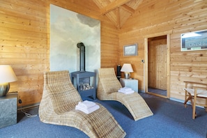 Ein Holzblockhaus-Interieur mit zwei Korbsesseln, einem Holzofen und einem gerahmten Bild an der Wand.