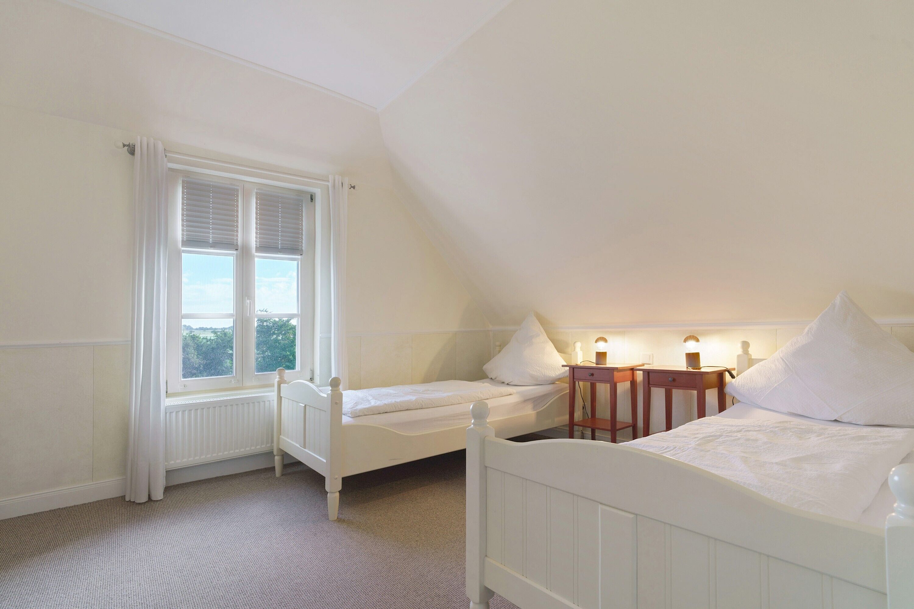 Une chambre avec deux lits simples, une fenêtre avec des rideaux, une table de chevet avec une lampe et un radiateur.