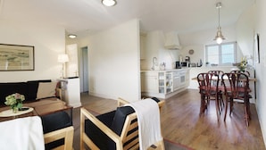 Amplia sala de estar con una mesa de comedor, sillas, un sofá, una cocina al fondo y un ventanal grande.