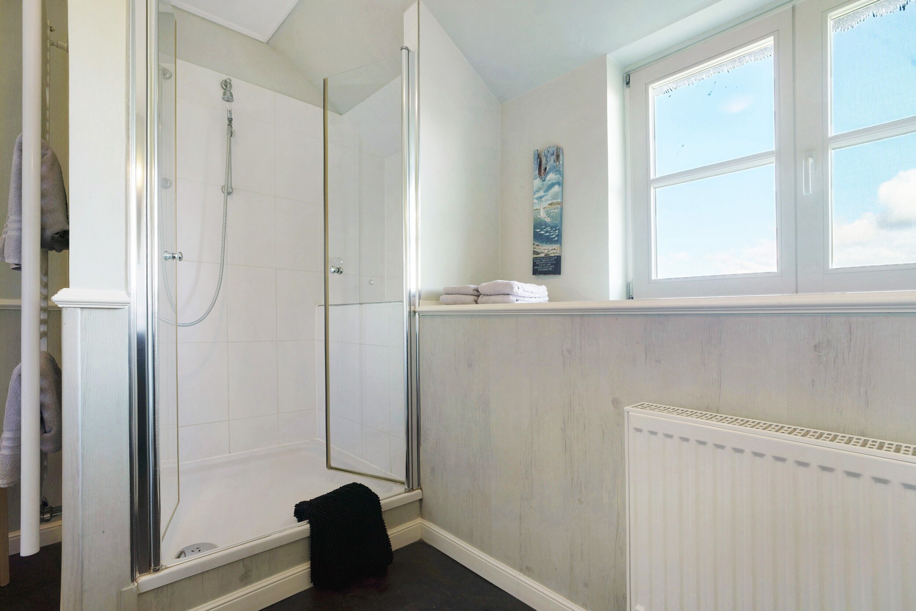Een badkamer met een douchecabine van glas, een raam met uitzicht en een radiator.