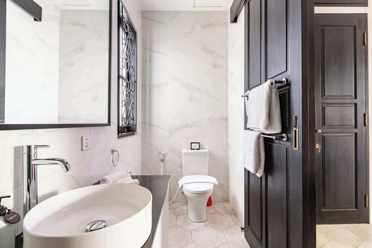 Un baño moderno con un lavamanos grande blanco, un inodoro y armarios de madera oscura.