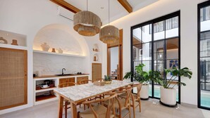 A modern kitchen with a marble countertop, wooden chairs, and hanging light fixtures.