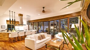 A modern living room with a white sofa, wooden coffee table, and a dining area with bar stools.