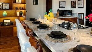 A modern kitchen with a long island, wooden shelves, and a dining area with a white bench.