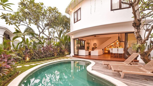 A modern house with a swimming pool, outdoor seating, and lush greenery.