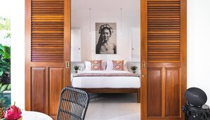 A bedroom with a bed, a chair, a bedside table, a wall-mounted picture, and a door with wooden panels.