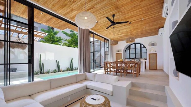 A modern living room with a large sofa, a dining area, and a view of a swimming pool.