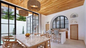 A modern dining area with a marble table, wooden chairs, and a kitchen in the background.