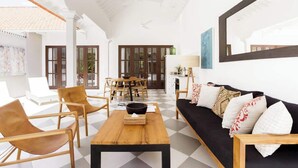 A spacious living area with a checkered floor, a wooden coffee table, a black sofa with patterned cushions, and a dining area in the background.