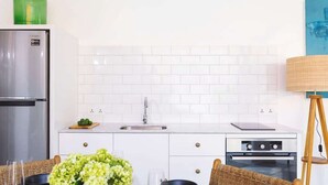 A modern kitchen with white cabinets, a stainless steel refrigerator, a sink, and an oven.