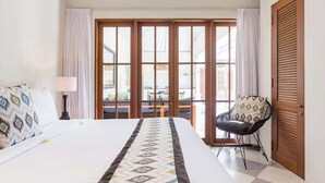 A hotel room with a large bed, a chair, a wooden door, and a view of the outside.