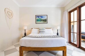 A neatly made bed with a white bedspread and decorative pillows, a framed picture of a beach scene on the wall, and a large window with curtains on the right. - Unwind at Seminyak Pool Villa 1Min Walk to Center (Kerobokan Kelod)