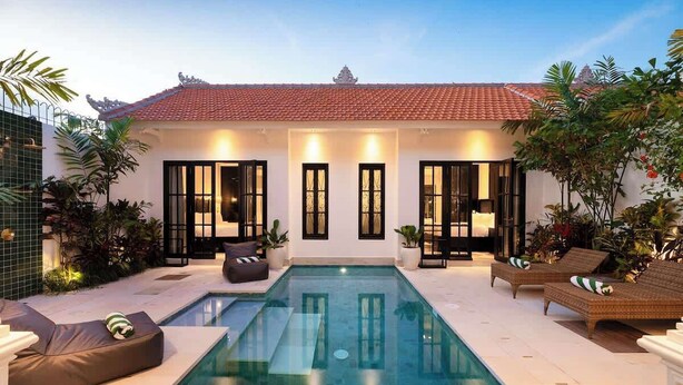 A poolside area with a swimming pool, lounge chairs, and a white building with a tiled roof. - 2BR Villa Martini 1 Spacious Walk to FINNS Beach (Dalung)