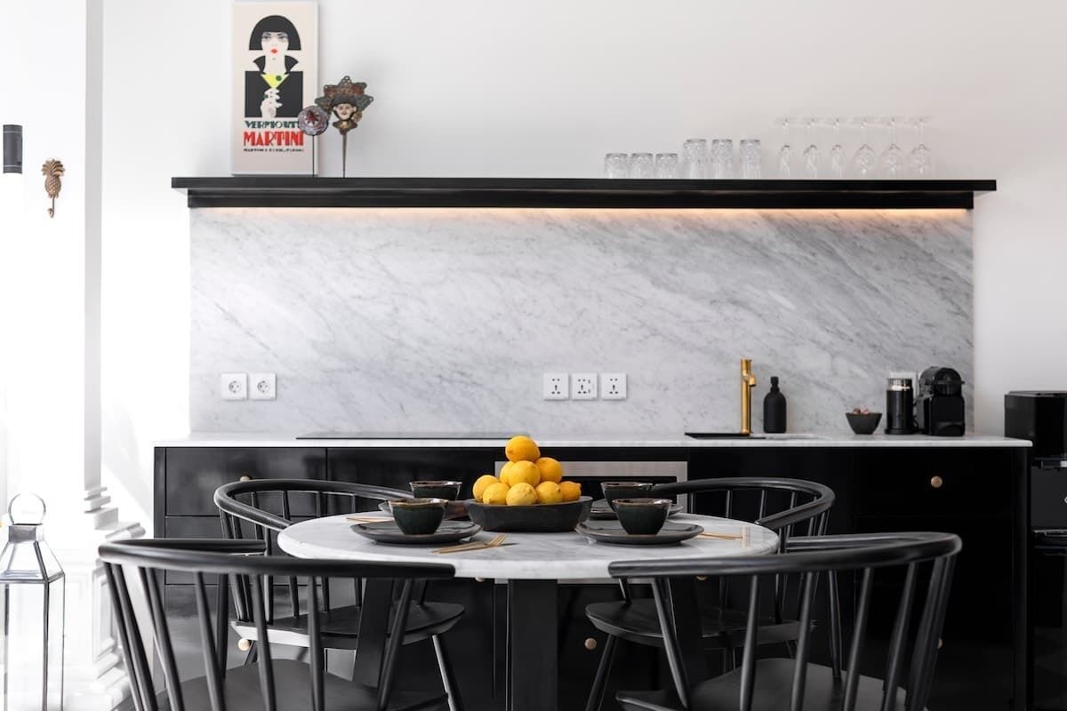 Une cuisine moderne avec un plan de travail en marbre, des chaises noires et un panier de fruits.