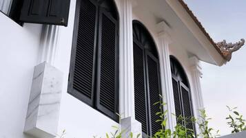 Un bâtiment aux murs blancs et aux volets noirs, présentant un style architectural traditionnel avec des fenêtres en arc de cercle et un élément décoratif sur le toit.