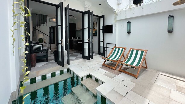 Zona exterior moderna amb una piscina, dues cadiretes de fusta i una escala que condueix a un nivell superior.