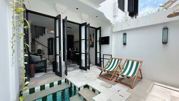 Un espace extérieur moderne doté d’une piscine, de deux chaises longues en bois et d’un escalier menant à un niveau supérieur.