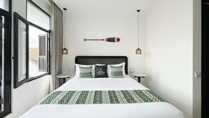Habitació d'hotel amb un llit gran, un capçal, una taula de nit, una làmpada i una finestra amb cortines.