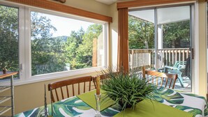 A dining area with a table set for two, a potted plant, and a view of the outdoors through large windows. - Bridges Resort Condo with Pools, Hot Tub & Sugarbush Access (Warren)