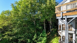 A multi-story building with a balcony, surrounded by dense green forest. - Bridges Resort Condo with Pools, Hot Tub & Sugarbush Access (Warren)
