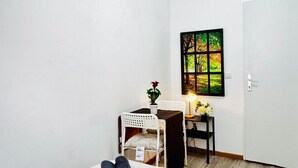 A small room with a white wall, a door, a window with a view of trees, a white chair, a small table with a plant, and a lamp. - Affordable Room in Shared Apt. Close to Stadthalle (Vienna)