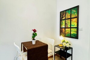 Um quarto com uma mesa, cadeiras, uma planta em vaso, uma mesinha com flores e um quadro na parede.