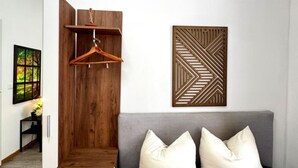 A room with a grey sofa, two white pillows, a wooden coat rack, and a geometric wall decoration. - Affordable Room in Shared Apt. Close to Stadthalle (Vienna)