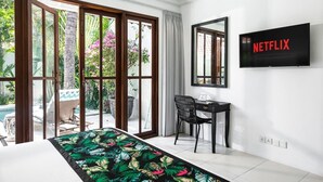 Ein modernes Hotelzimmer mit einem großen Bett, einem Schreibtisch, einem Stuhl, einem Fernseher und Blick auf Pool und Garten.