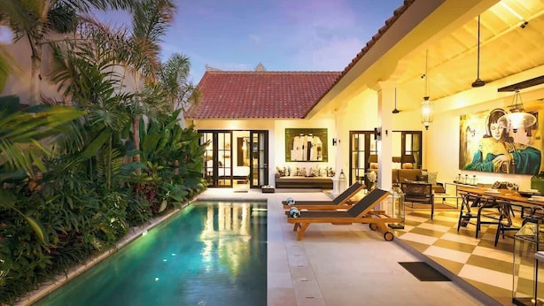 A poolside area with lounge chairs, a dining table, and a mural on the wall. - Villa Nago · 2 King Suites · Walk to Potato Head (Kerobokan Kelod)
