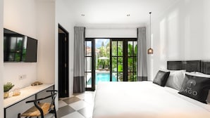 A modern hotel room with a large bed, a desk with a chair, a TV mounted on the wall, and a view of a swimming pool through a glass door. - Villa Nago · 2 King Suites · Walk to Potato Head (Kerobokan Kelod)