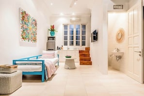 Une chambre à coucher avec un lit, une petite table, une fenêtre et une salle de bain équipée d’un lavabo et d’un miroir.