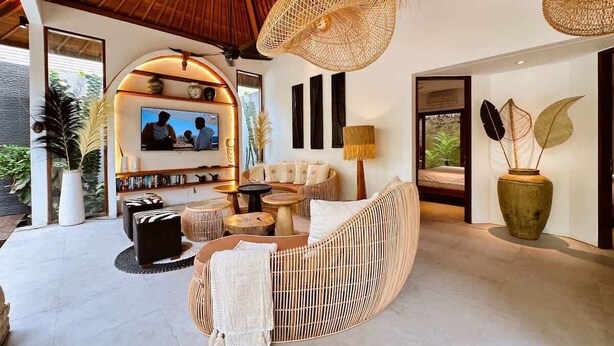 A spacious living area with a curved sofa, a television, and a large window overlooking greenery. - Tropical Cozy 4BR Villa Pacha Seminyak Up to 12pax (Seminyak)