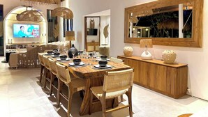A modern dining area with a long wooden table set for six, surrounded by wicker chairs. A wooden console table with decorative items is against the wall. - Tropical Cozy 4BR Villa Pacha Seminyak Up to 12pax (Seminyak)