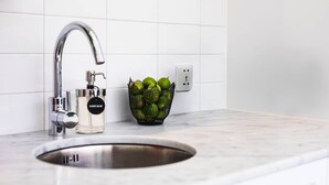 A kitchen sink with a modern faucet, a bottle of hand soap, and a bowl of green fruits on the counter. - Cozy 1BR Villa Pandi - Walk to Eat Street Seminyak (Seminyak)