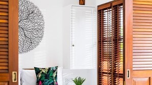 A bedroom with a wooden bed frame, a white mattress, a tropical patterned pillow, a small potted plant, and a wall art piece. - Cozy 1BR Villa Pandi - Walk to Eat Street Seminyak (Seminyak)