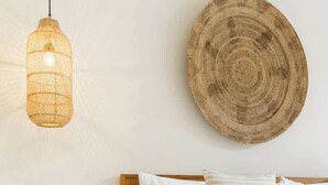 A bedroom with a wooden bed, white bedding, a woven wall hanging, a small bedside table with a plant, and a hanging light fixture. - Exclusive 2BR I Walk to Seminyak Mall & the Beach (Kerobokan Kelod)