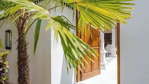 A white-walled building with a wooden door and a palm tree in the foreground. - Exclusive 2BR I Walk to Seminyak Mall & the Beach (Kerobokan Kelod)