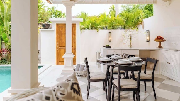 A dining area with a pool view, white walls, and tropical plants. - Exclusive 2BR I Walk to Seminyak Mall & the Beach (Kerobokan Kelod)