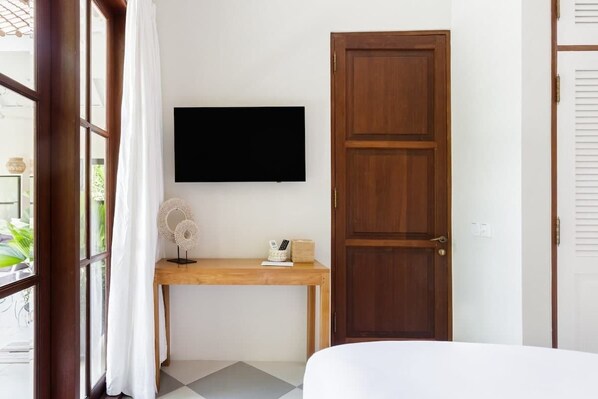 A room with a bed, a wooden desk with a flat-screen TV, a door, and a window with curtains.