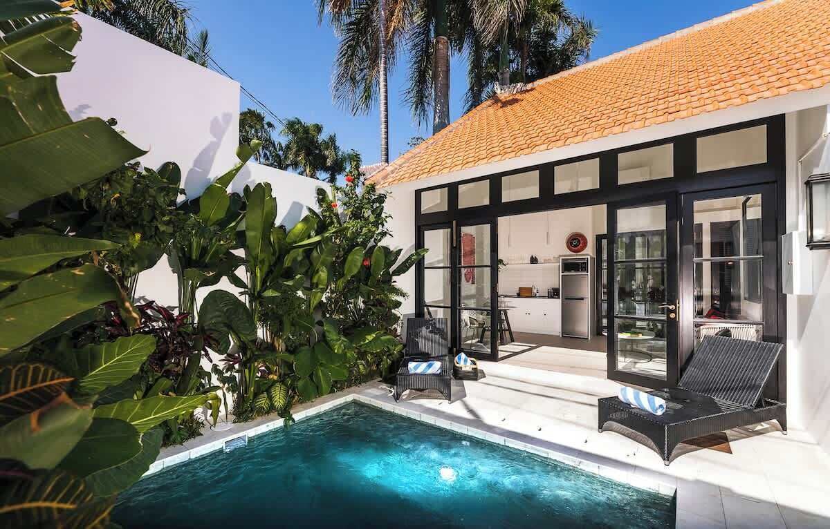 A modern house with a swimming pool, large windows, and tropical plants.