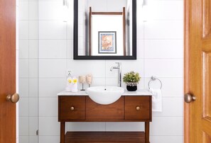 A bathroom with a white sink, wooden vanity, and a mirror with a framed picture. - Walk around Seminyak Petitenget from 1BR PoolVilla (Kerobokan Kelod)