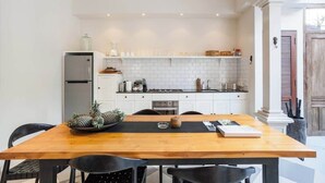 A modern kitchen with white cabinets, a wooden dining table, and a refrigerator. - Comfort 3BR Soleh Walk to Shops & Beach Seminyak (Kerobokan Kelod)