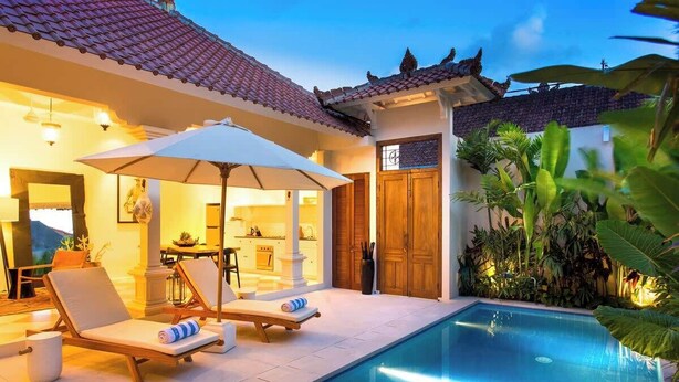 A poolside area with lounge chairs and an umbrella, a tiled pool, and a traditional building with a tiled roof. - Comfort 3BR Soleh Walk to Shops & Beach Seminyak (Kerobokan Kelod)