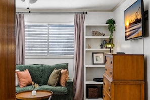 A living room with a green sofa, a wooden cabinet, a TV on the wall, and a window with curtains.