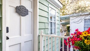 A white door with a welcome sign, a green house exterior, and a porch with colorful flowers. - 4 Blocks to Beach! • Historic Cottage • 5mins Strand/Port w Driveway Parking (Galveston)
