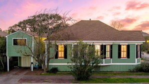 A two-story house with a green exterior, a garage, and a small porch. - 4 Blocks to Beach! • Historic Cottage • 5mins Strand/Port w Driveway Parking (Galveston)