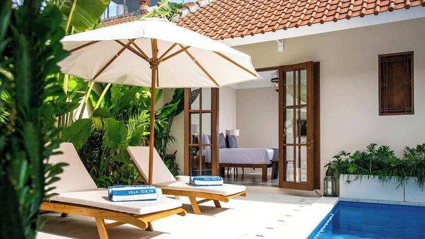 A poolside area with two lounge chairs, a table, and an umbrella.