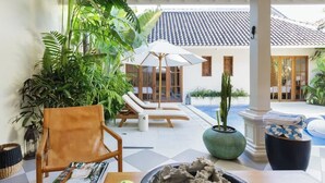 A sunlit outdoor lounge area with a pool, lounge chairs, and potted plants.