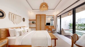 A modern bedroom with a large bed, a wooden desk, a small seating area, and a view of a pool.